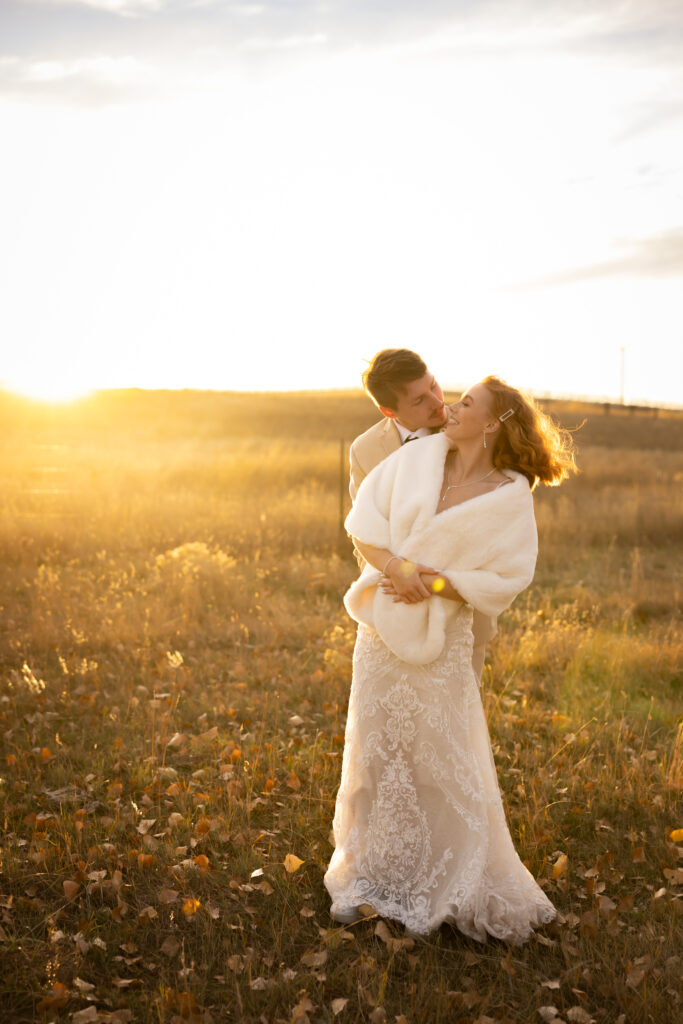 Newlywed couple sharing an intimate moment in a golden prairie at sunset.